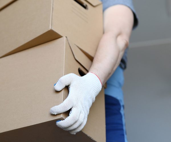 Man in work clothes and gloves carries cardboard boxes. Folding boxes. Moving waiting for loading service. Things are collected for moving. Collection goods in warehouse online store during quarantine